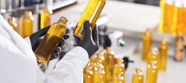 Manufacturing concept. Factory worker holding two glass bottles with yellow liquid comparing quality between them. Factory process of production shampoo. Technology, innovation and scientific concept